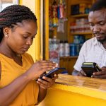 Customer using her phone at a mobile money agent counter in Uganda