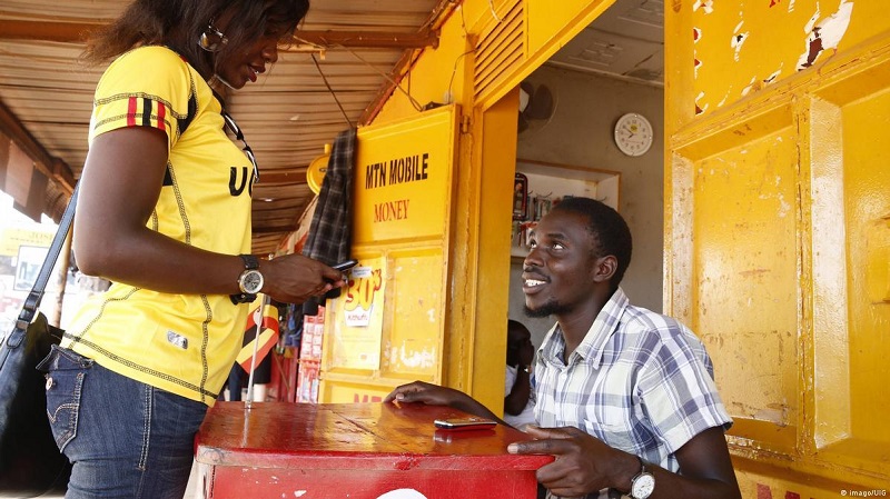 Customer using her phone at a mobile money agent counter in Uganda